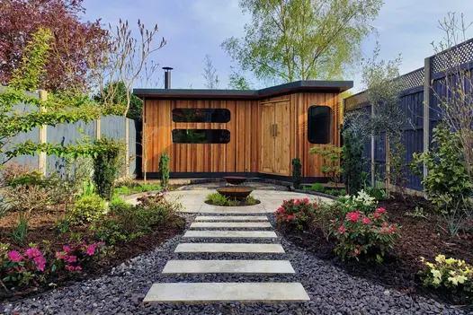 Rectangle Cream Porcelain stepping stone path set amongst slate chippings and flower beds leading to a cedar garden building.