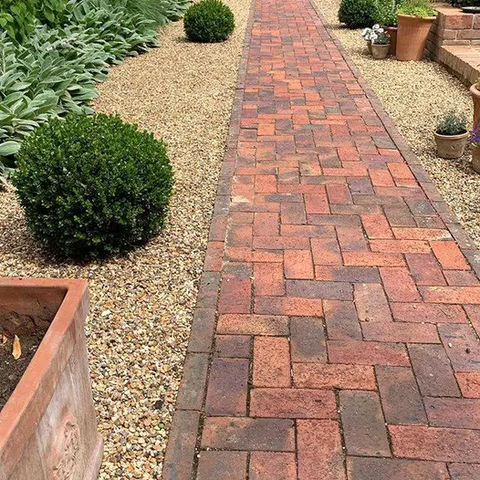 Topiary bushes and light pebbles surround dorset antique clay paver path with a red brick step leading up to another level.