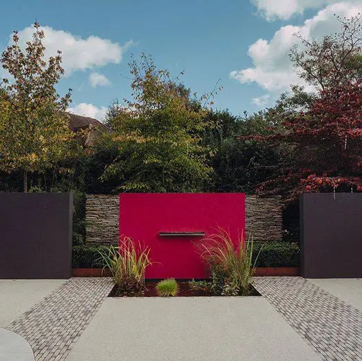 Strips of Silver Grey Multi clay pavers run either side of water feature with red wall and planted pond. Built Langdale Landscapes.