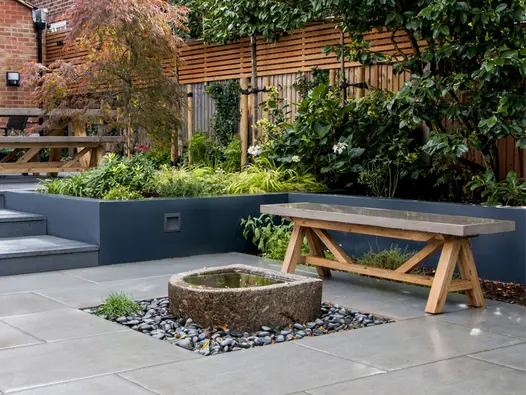 D-shaped raised stone pond in square black-cobbled surround, set into Trendy Black Porcelain paving. By NLG Landscaping.