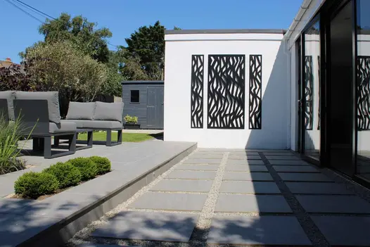 Staggered slabs set among pebbles lead to a long step up to a patio of Kandla grey porcelain paving, featuring modern outdoor furniture.