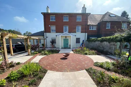 Garden with large bed in each corner, set around large circle of Old English Clay Pavers with metal bowl sculpture in centre.