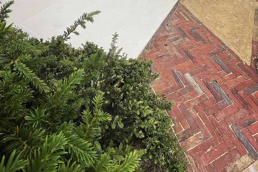 Next to evergreens, path of Old English Belgian bricks, laid herringbone pattern, abuts pale paving and bound gravel areas.