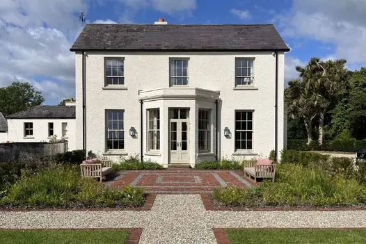Paved square of Old English clay pavers with pebble detailing and 2 benches fronts Symmetrical white-painted Georgian house.