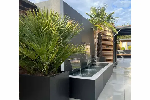 3 tier water feature uses opium black designclad for wall and water trough, palm trees sit either side.