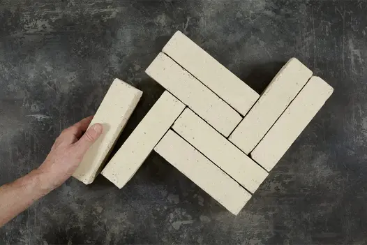 Hand holding a clay paver brick in Oslo, alongside 7 other clay paving bricks laid out in herringbone shape.
