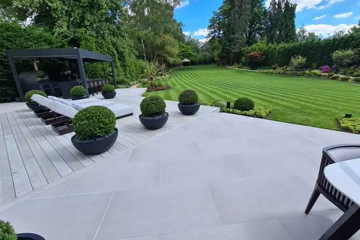 Patio of Luna outdoor decking laid with toning paving, with sun loungers, potted shrubs and outdoor bar, next to huge striped lawn.