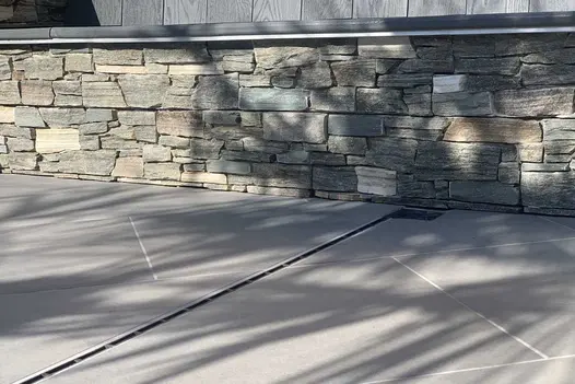 Florence Storm Porcelain slabs laid in an angled bond pattern butting up to a natural stone clad wall.