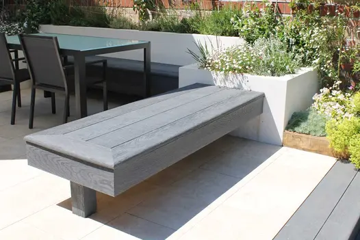 Bench of Basalt Millboard Decking bullnose boards attached to square raised bed forms one side of Inbuilt seating on patio.