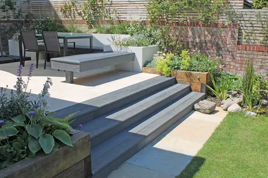 3 steps of Millboard bullnose rise between wooden sleeper beds to patio with matching inbuilt bench and dining set in walled garden.