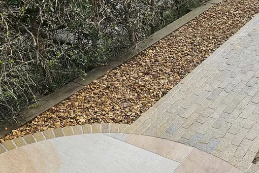 Antique Yellow Stone Pavers form a path from a stone circle, flanked by pebbles on each side and bordered by plants used as hedges on the left.