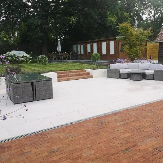 Two sets of rattan outdoor furniture sits on light paving, with slot drain running between patio and romsey antique clay pavers.