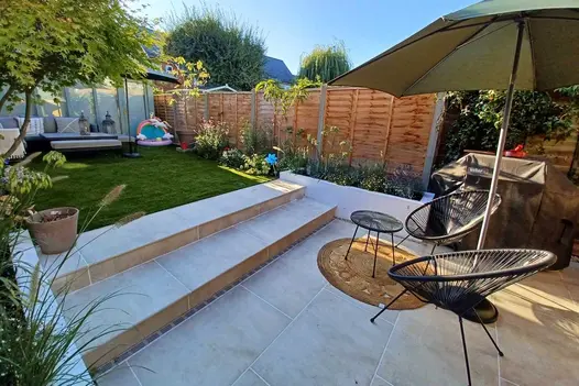 Small back garden with Cream porcelain patio and steps leading up to a raised artificial lawn and comfortable seating area.