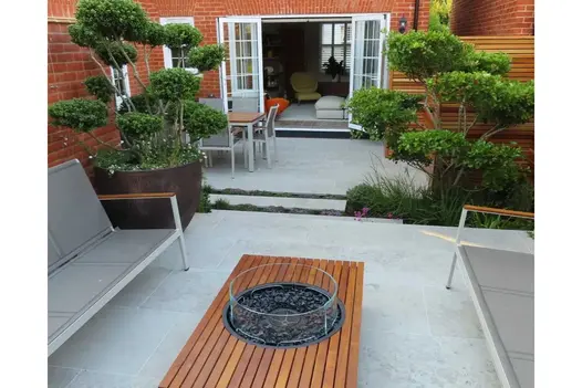 French doors open onto Jura grey limestone paved garden with table and metal benches. Design by Tom Hill. Built by PDGroundscape.