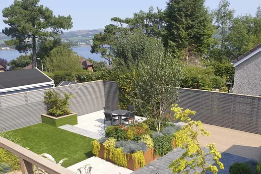 Garden with 2 raised beds, artificial lawn and variety of paved surfaces surrounded by fencing of Pebble grey composite battens.