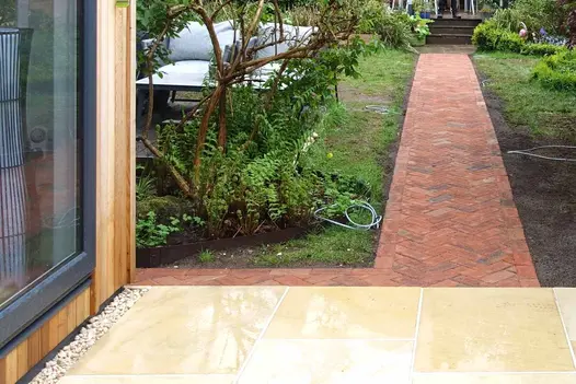 short path of romsey antique clay pavers in herringbone style lead to steps, away from wet sandstone patio.