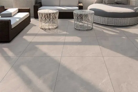 Modern outdoor space using Piazza Grey Porcelain Paving, with rattan garden furniture and smooth tiles in a soft grey tone.