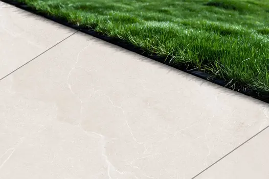 Edge of a porcelain patio using Piazza White, showing the pale marble-effect surface alongside a vibrant lawn.