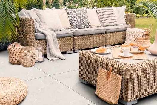 Piazza White porcelain paving in a relaxed garden lounge setting with rattan furniture and neutral-toned decor.