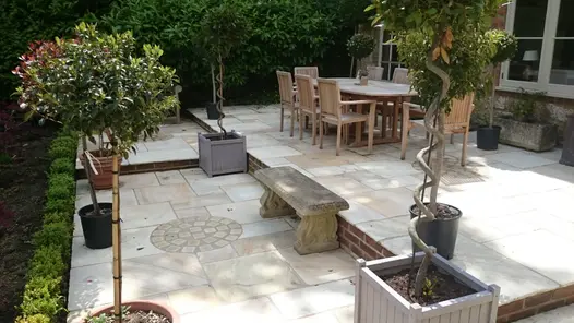 stone bench sits on bottom level of 2 tire patio using tumbled mint sandstone paving with a dining table for 8 people on the top.