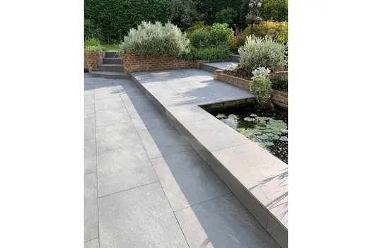 Mature country garden with paved terraces and raised brick flower beds and sunken pond on the first terrace.