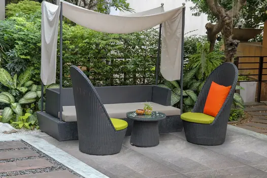 Tall wicker garden chairs and sofa covered by a shade sail and sitting on top of a Platinum Grey porcelain patio.