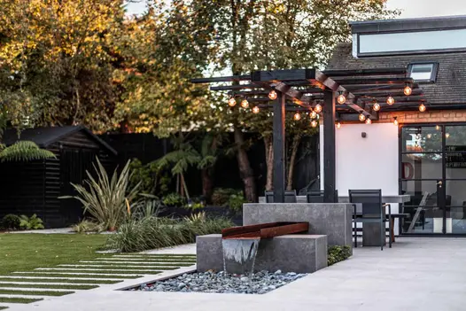 Steel corten trough flows water into pebbled area with raised walls clad with vulcano ceniza designclad in unique feature.