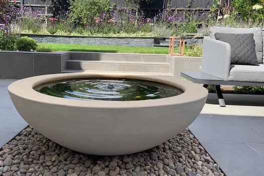 Water feature on top of pebbles shows Steel Grey Porcelain Outdoor steps in the background, leading to lawn.