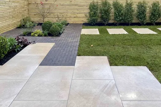 Porcelain patio leading into dark clay pavers and a porcelain stepping stone path cutting through a lawn.