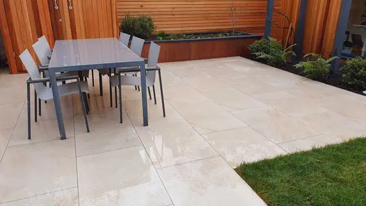 Wet light coloured porcelain patio with a rectangle six seater dining set against a back drop of cedar screen and matching storage unit.