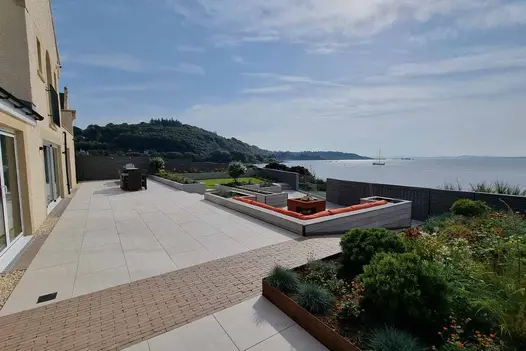 Cream-coloured house with wide Faro porcelain and clay paver terrace  on 2 levels with view of sea inlet.