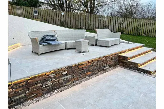 Garden steps made of Silver Grey Porcelain, leading down from elevated outdoor lounge area with rattan furniture.