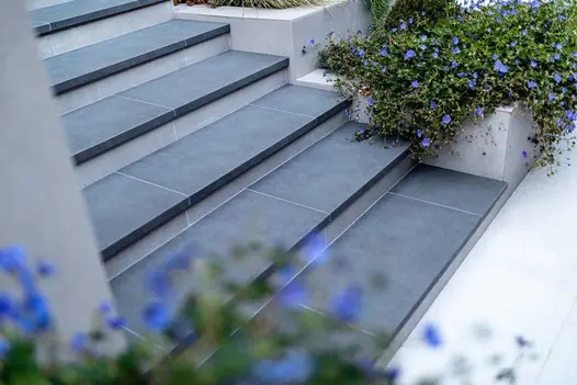 Steel Grey porcelain steps with 20mm downstand, next to DesignClad-faced stepped planters. Design by Gardens of the Future. 