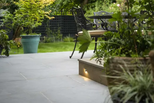 Dining set on Florence Storm porcelain 900x600 tiles, with lawn and fence beyond. Design by Jaki Grosvenor. Laid by Acacia Gardens.