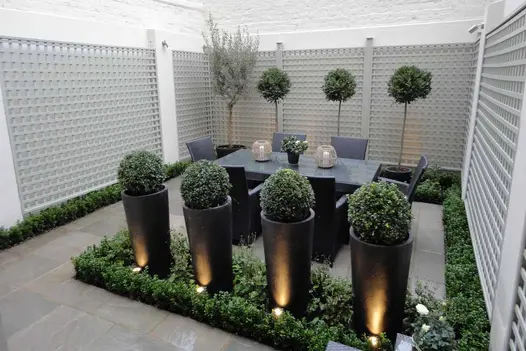 4 topiary balls in tall pots in tiny courtyard paved with Kandla Grey sandstone slabs, with dining table and clipped trees.