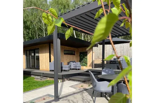 Large garden room with veranda, seen through Proteus Grey aluminium pergola with louvred roof. Design by Chameleon Landscaping.