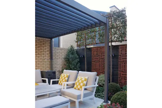 Outdoor armchairs under Proteus grey aluminium pergola next to house wall and fence. Installed by East London Garden Design.
