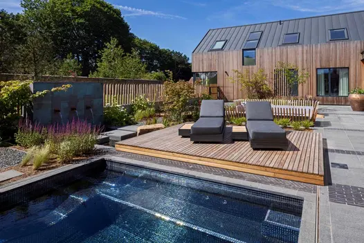 Modern wooden house with large patio and raised decking next to pond edged with Black Granite coping stones with pencil round edge.