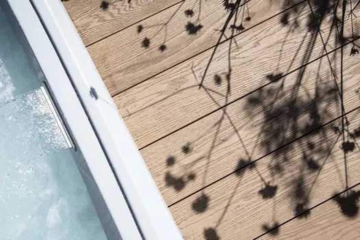 Close-up of Golden Oak Millboard decking planks meeting white edge of water feature at right angles. Design by Rachel Goozee.