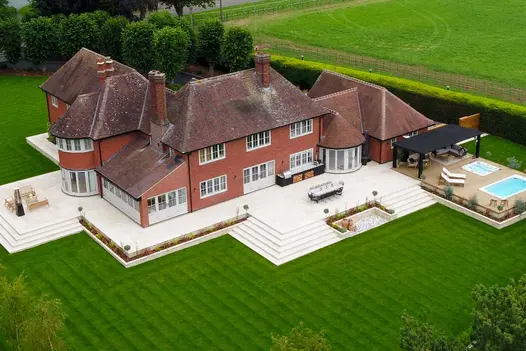 Aerial view of huge house surrounded by patio with Beige sawn sandstone bullnose steps descending on all sides to striped lawn.