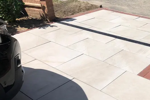 Ash beige porcelain laid in 900x600 large rectangles on a residential driveway with a black plastic channel drain cutting across.