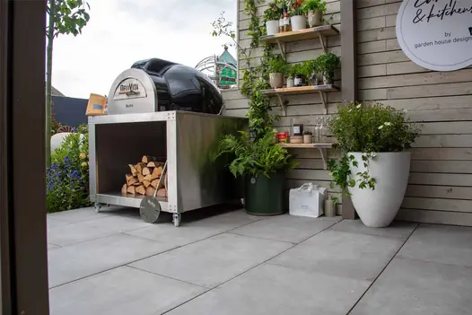Trade stand paved with Venetian Grey Porcelain paving slabs, with wood-fired pizza oven, planters, and potted plants on shelves.