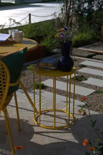 Yellow metal furniture sits on egyptian beige limestone pavers at RHS Tatton Park Chelsea Flower Show.