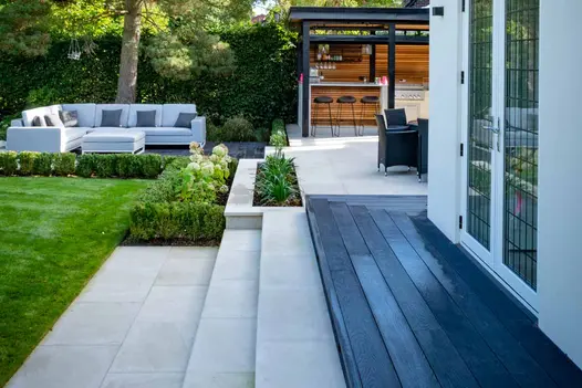 Bar and dining area in the background with light patio and steps leading up to narrow burnt cedar millboard decking area.