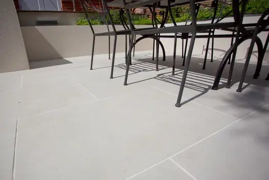 Black metal furniture casts shadows onto Beige smooth sandstone paving bounded by low wall. Design by Robert Straver.