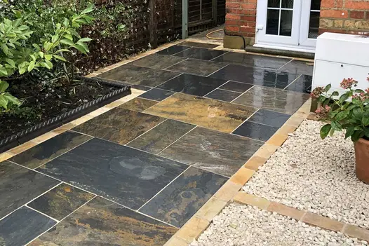 Wide path showing rich colour of wet Rustic Slate patio pack paving between planted bed of equal width and gravel driveway.