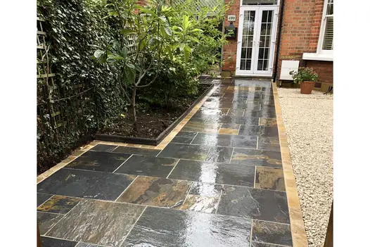 Wide rustic slate path leads to french doors of period house between border with Victorian edging and white gravelled area with pot.