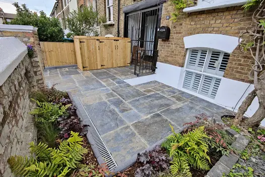 View from front of house showing Rustic Slate Paving leading to bin store next to gated french doors, flowerbeds surround.
