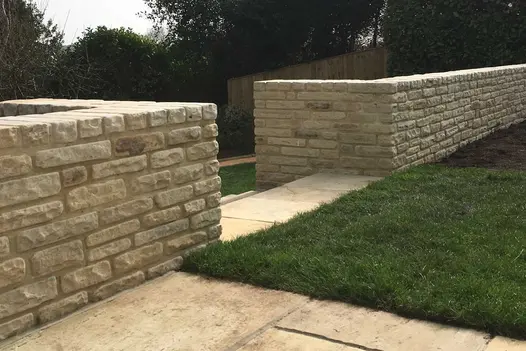 2 Mint sandstone walls edge lawn of paved area. and meet at gap, turning right angles to create flanking walls to steps.