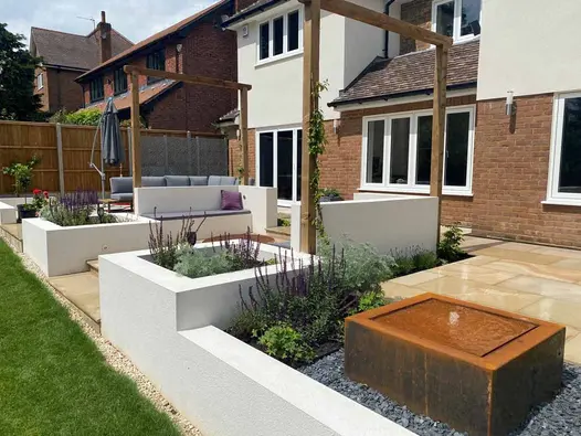 Rear of brick and render suburban house with Light Buff sawn sandstone patio and white raised beds and inbuilt benches.